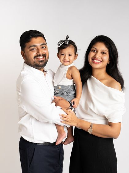 A classic and cheerful family-of-three portrait. Their coordinated black and white outfits give this studio photo a modern and timeless feel.