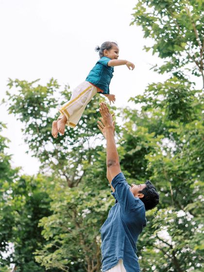 A father tossing his son in the air. The joy and trust in this moment are beautifully captured against the green trees.