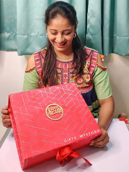 Here I am with one of our premium red Diwali hampers. The box itself is a keepsake, and it’s filled with festive items like a lotus diya, shubh labh hangings, and delicious treats.