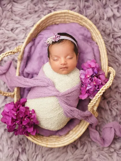 A newborn girl swaddled in a basket, surrounded by vibrant purple flowers. Using a strong color theme can create a very striking and beautiful portrait.