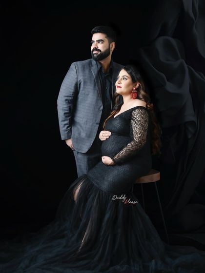 A formal couple's portrait against a dark backdrop. The expectant mother wears a beautiful black lace gown, creating a timeless and elegant look for their family maternity photoshoot.