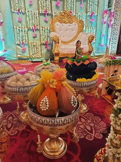 We work with both gold and silver-toned platters to match your event's theme. This silver platter arrangement for a baby shower features colorful potli bags and a unique doll seated on a lotus-shaped coconut stack.