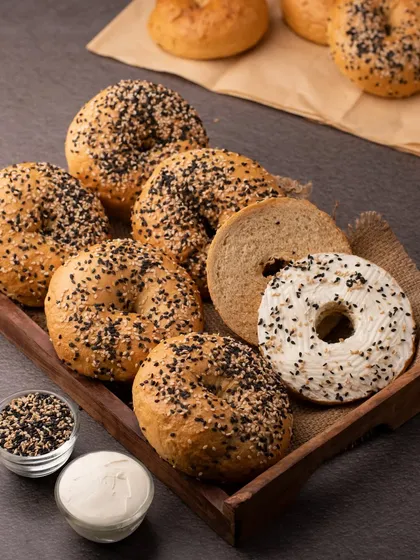 A tray of freshly baked bagels, some plain and some with cream cheese and sesame seeds. This shot showcases the texture and variety of the product.