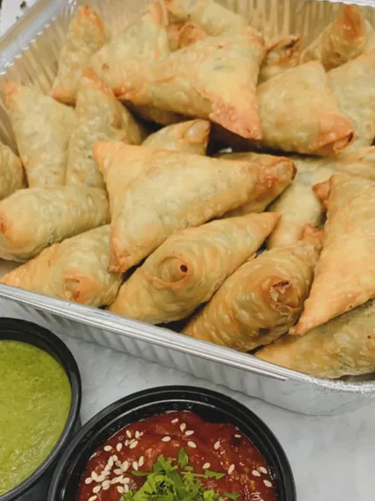 A catering tray full of freshly fried Chicken Irani Samosas, served with mint and sweet chili chutneys. I can prepare these in bulk for large parties.