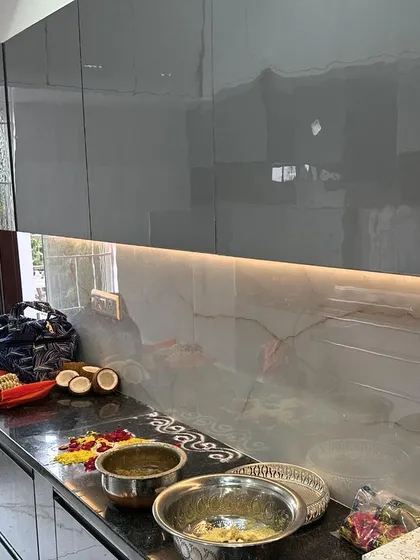 A finished modular kitchen with high-gloss grey cabinets and under-cabinet lighting, ready for use during a housewarming ceremony. The sleek, handleless design provides a clean and contemporary look.