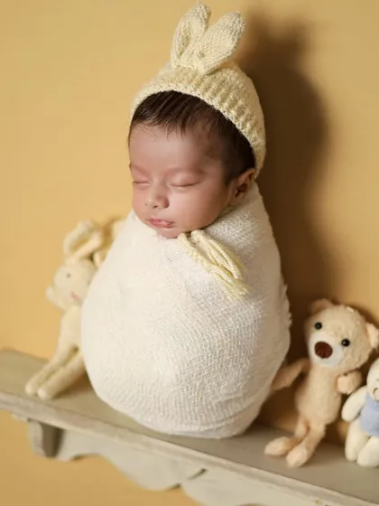 A sweet 'potato sack' wrap pose on a little shelf with teddy bears. This pose keeps the baby snug and secure, and it's always a parent favorite.