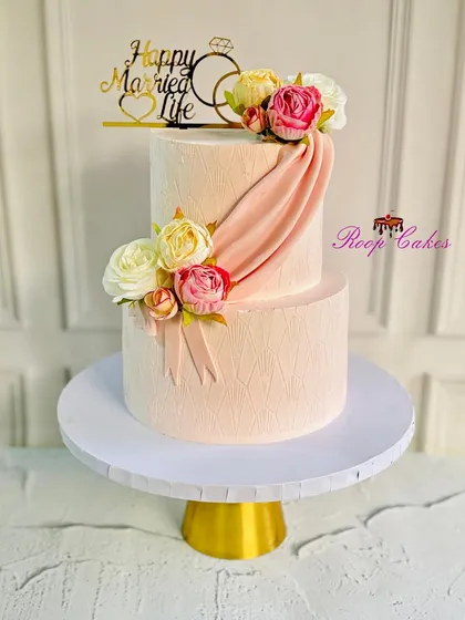 A sweet beginning to a beautiful forever. This two-tier anniversary cake in a soft pink hue features elegant draping and is adorned with fresh flowers for a classic, romantic look.