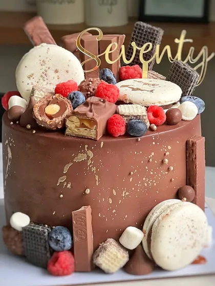 This chocolate overload cake was made for a 70th birthday. It's piled high with macarons, berries, and a variety of chocolate bars like KitKat and Ferrero Rocher.