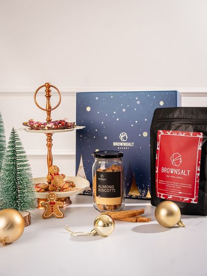 A full view of one of our curated Christmas hampers. It includes our Xmas Special Granola, Almond Biscotti, and a tiered stand with gingerbread men and chocolate bark, all ready to be gifted in our signature blue box.