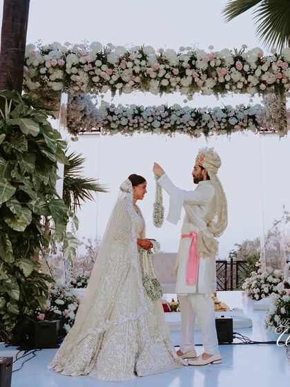 An elegant varmala exchange at a sunset ceremony. The clean, white decor with lush floral arrangements creates a sophisticated and timeless look for a modern Indian wedding.