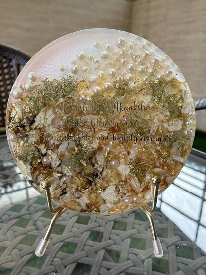 An 8-inch round display frame with preserved varmala flowers. The simple and elegant design, personalized with the couple's names, makes this a beautiful and timeless keepsake.