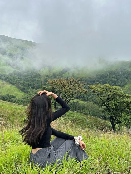 A traveler sitting in the lush green grass of Netravathi peak, enjoying the view.