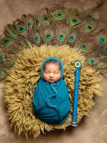 This is one of my favorite poses for the Krishna theme, showing the baby swaddled snugly in a beautiful blue wrap, resting on a textured nest with a fan of peacock feathers behind them.