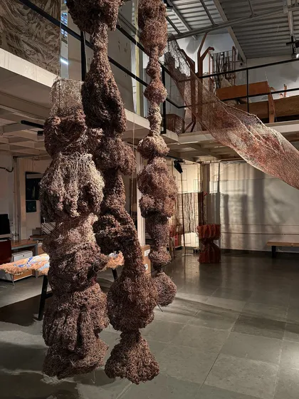 Hanging sculptures from the 'Cu+Fibers' exhibition. These dense, organic forms are created by crocheting and wrapping natural fibers, resulting in a series of unique, tactile objects.