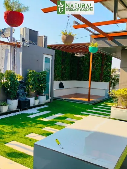 A daytime view of the Sonipat project, showing the pergola, artificial lawn, and planters under bright sunlight.