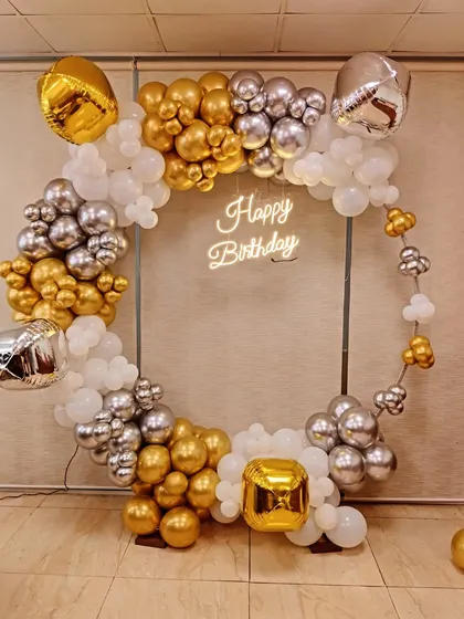 For a modern and chic birthday celebration, I design statement pieces like this circular frame with a custom 'Happy Birthday' neon sign. The organic balloon garland in gold, silver, and white adds a touch of elegance and is perfect for photos.