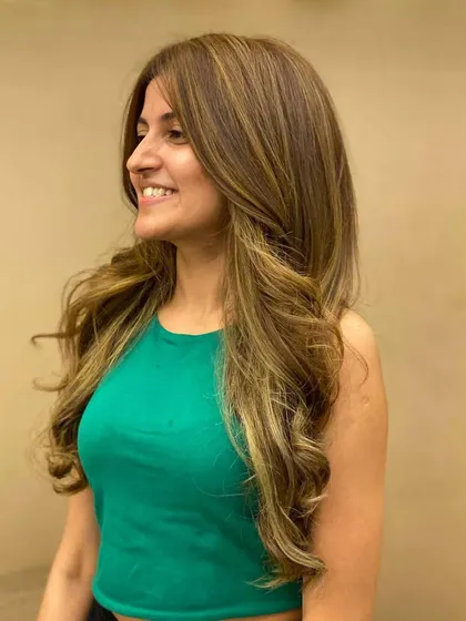 A smiling client with her new hair color. The highlights and soft waves give her a fresh, radiant look.