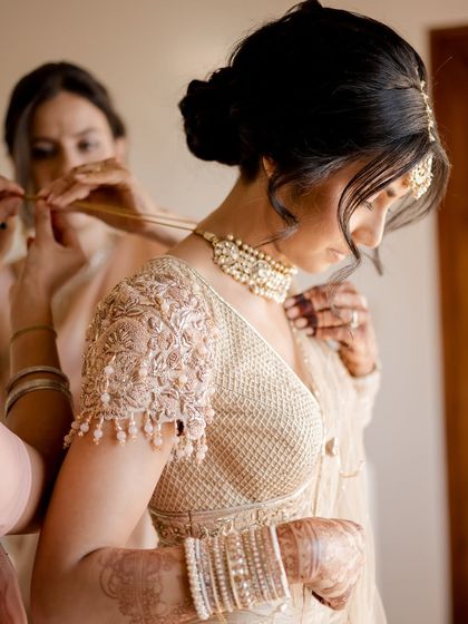 The final touches. A getting-ready shot of the bride as her pearl choker is fastened. The intricate threadwork on her blouse sleeve is a testament to the craftsmanship of her Tarun Tahiliani outfit.