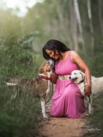 A duplicate of image 65, this image perfectly captures the affectionate bond between a pet parent and her rescue dogs. The natural, green environment and soft lighting create a peaceful atmosphere for this beautiful interaction.