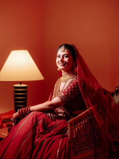 A happy, relaxed portrait of the bride seated in a warmly lit room. Her genuine smile and the soft red tones create a welcoming and intimate image.