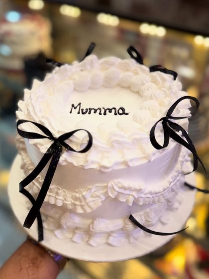 A pretty two-tier cake with black ribbon bows. The design is simple yet chic, making it a versatile choice for a variety of celebrations, from birthdays to anniversaries.
