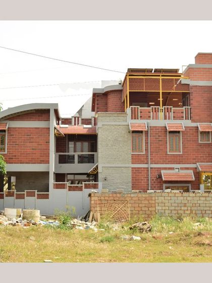 An exterior view of the Kavitha and Ravishankar residence, showing multiple levels, curved elements, and a rooftop terrace, all built with eco-sensitive materials.