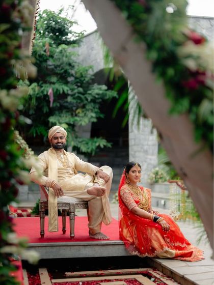 A royal portrait of a couple. The bride is seated in a vibrant red lehenga, while the groom relaxes in a custom-made golden silk sherwani and dhoti, a perfect example of our bespoke couple's couture.