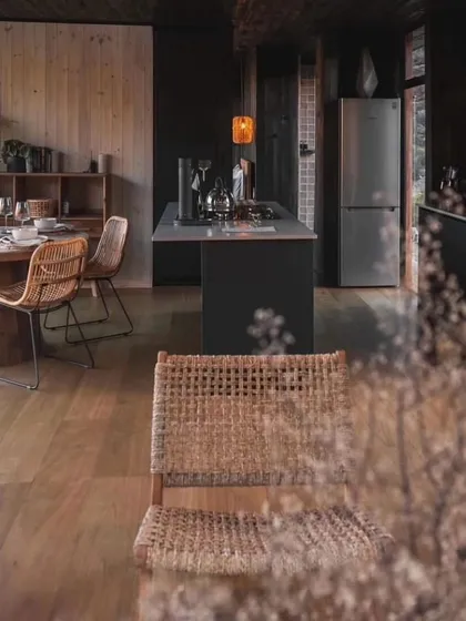 The interior of this cabin features a dark, moody aesthetic with natural wood and woven furniture. It’s a perfect example of how we can create a cozy, sophisticated atmosphere within a modular space.