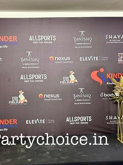 We create custom-printed backdrops that prominently feature event sponsors and partners. This step-and-repeat banner is framed with elegant gold and white floral arrangements for a polished look.