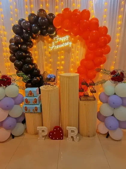 An anniversary decoration with a unique half-and-half balloon arch in black and orange. The light-up initials "P" and "R" add a personalized touch for the couple.