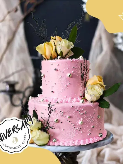 A romantic two-tier anniversary cake in pink, decorated with fresh yellow roses and silver sprinkles. A beautiful way to celebrate a special milestone.