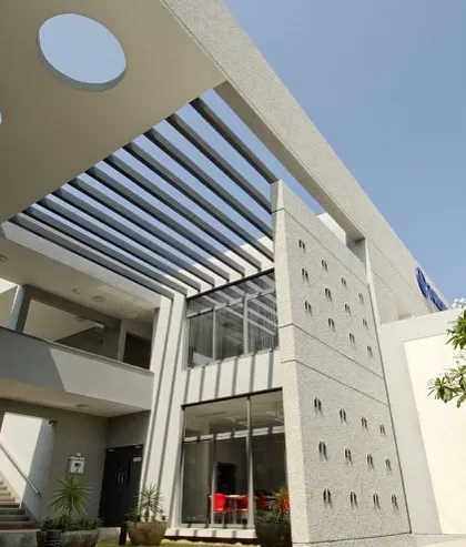 An exterior view of the Torishima Pumps corporate campus in Hosakote. We designed the building with clean geometric lines, using textured concrete and a slatted pergola to create dynamic patterns of light and shadow. This approach demonstrates our focus on creating visually engaging facades in commercial architecture.