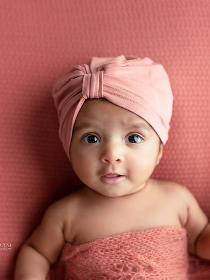 An older newborn with bright, expressive eyes, wearing a stylish pink turban. This portrait is full of personality and shows the beauty of capturing babies beyond the two-week mark.