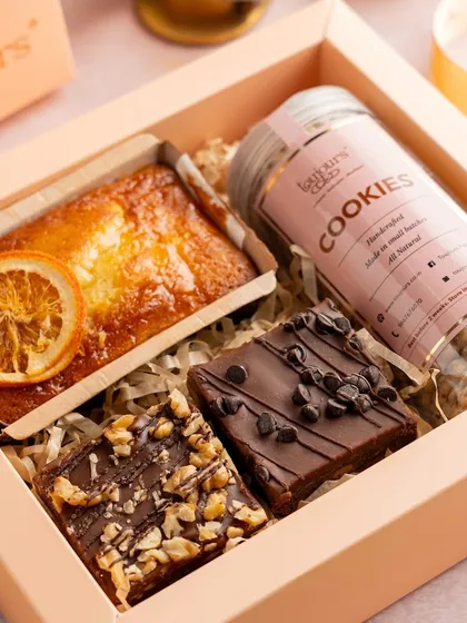 A charming gift box containing a mini orange tea cake, two different types of brownies, and a jar of mini cookies. It's a thoughtfully curated selection for a personal and sweet Diwali gesture.
