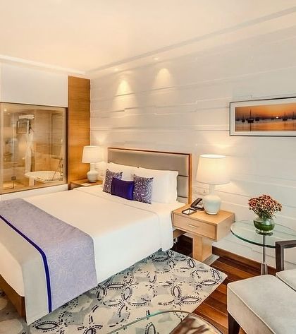 The bedroom in this Taj Vivanta Goa suite features a clean, modern aesthetic with our signature touch. The custom bed runner and cushions in shades of purple and blue echo the colors of a Goan sunset.
