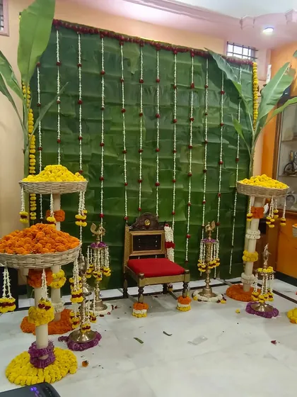 This full view shows a classic decor arrangement for a 'Devkarya' or baby shower at home. The wall of banana leaves, flanked by whole banana plants, creates a sacred and natural setting for the puja.