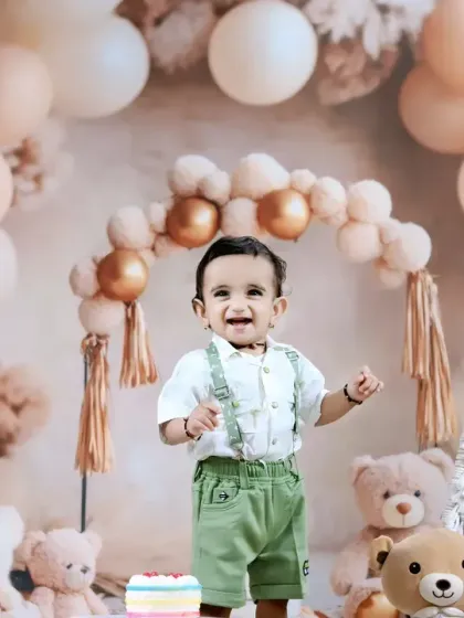 A happy toddler celebrates his birthday with a boho-themed setup, complete with teddy bears, pampas grass, and a colorful cake.