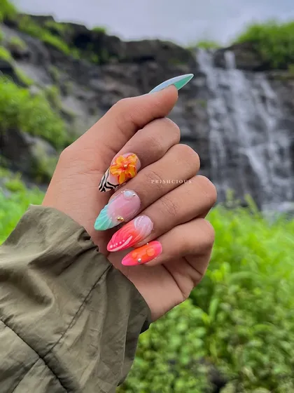 Admiring this beautiful set of vacation nails against a waterfall backdrop. This acrylic set features 3D flowers, bright colors, and a butterfly wing design.