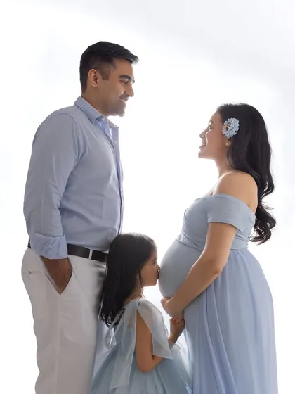 A sweet moment as a family prepares to grow. A little girl stands on her tiptoes to kiss her mother's pregnant belly, sharing her excitement for the new baby. This is a perfect example of a maternity shoot that includes the whole family.