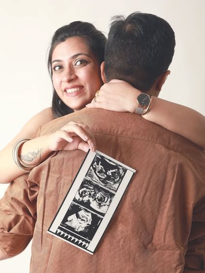 A creative announcement shot where the mom to be peeks over her partner's shoulder, holding the first ultrasound pictures. It's a fun and personal way to share your exciting news.