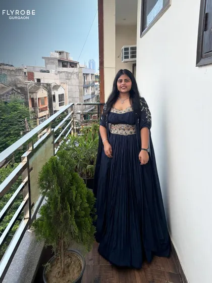 A full-length view of the navy blue pleated lehenga. The cape-like sleeves and embellished waistline make it a modern and stylish choice.