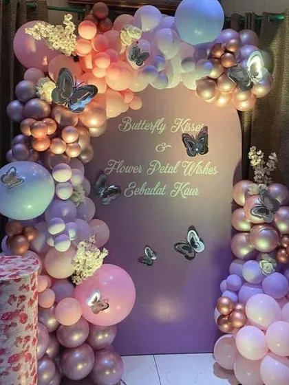 An elegant butterfly-themed party with a "Butterfly Kisses & Flower Petal Wishes" backdrop. The setup includes a pastel balloon arch and a themed pedestal.
