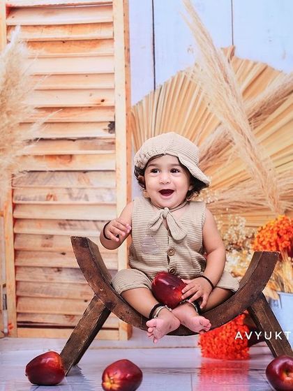 A baby boy in a rustic setup with apples and pampas grass.