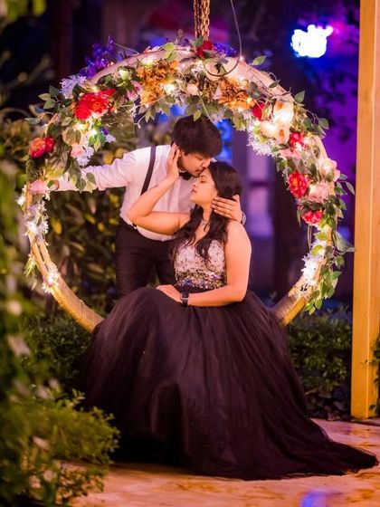 A romantic moment captured on a floral swing. The black ball gown and the partner's classic white shirt with suspenders create a timeless and elegant couple's portrait.