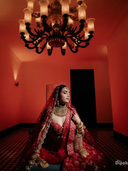 A bride in her magnificent red lehenga, captured in a moment of regal elegance under a chandelier.