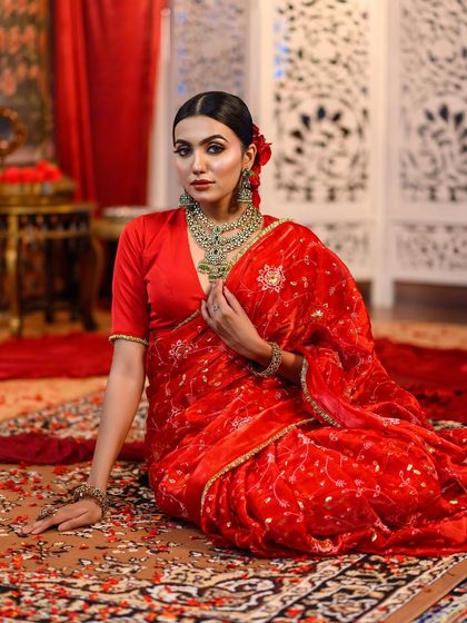 A full-length shot of a model in a stunning red saree, seated amidst a rich, traditional setting. This composition is perfect for editorial-style ethnic fashion shoots.