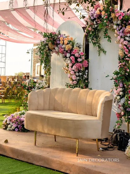 A beautiful photo spot where guests can capture memories. The plush velvet sofa is framed by a cascade of pastel roses and florals, set against a simple white backdrop for a touch of modern elegance.