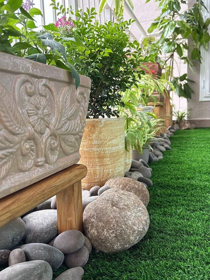 A close-up of the details that make a garden special. The carved planters and natural river stones add texture and an earthy feel, complementing the artificial grass and creating a polished look for this balcony garden.