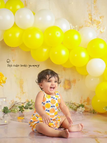 A moment of pure joy before the cake smash. The bright yellow balloon wall creates a cheerful and vibrant backdrop for this first birthday shoot.