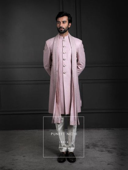 Blush tones meet timeless artistry. A sherwani in pink silk, layered with a fish-scale textured achkan and matching stole, becomes a portrait of soft elegance.